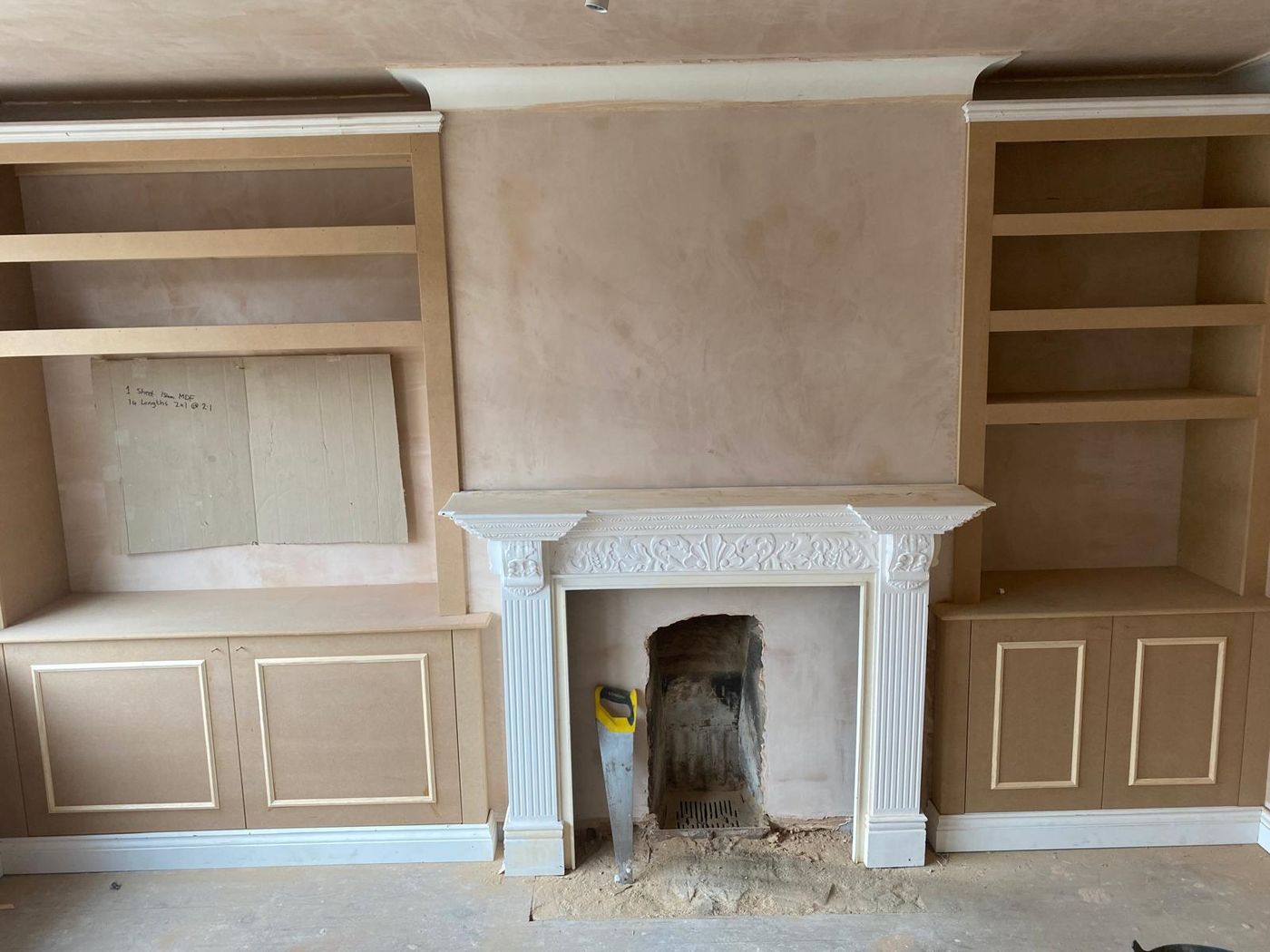 Built-in alcove cupboards with panelled doors and open shelving above on both sides of a fireplace with a carved surround, before painting