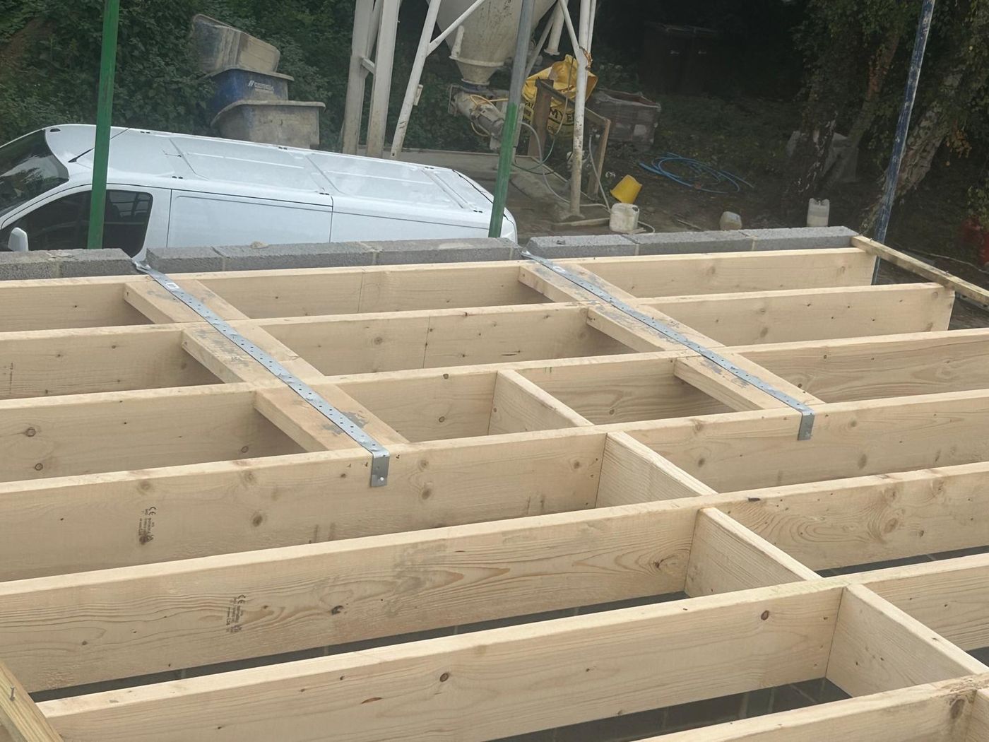 Grid of timber floor joists and noggins with metal restraint straps on a blockwork base
