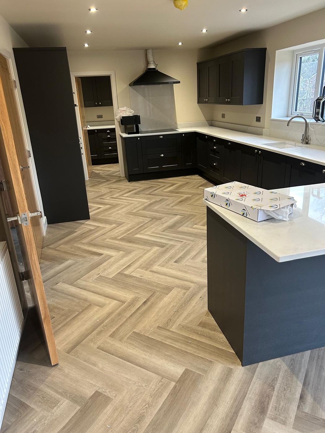 Dark grey shaker kitchen with tall housings, wall units, extractor and an island with a white quartz top on a herringbone floor