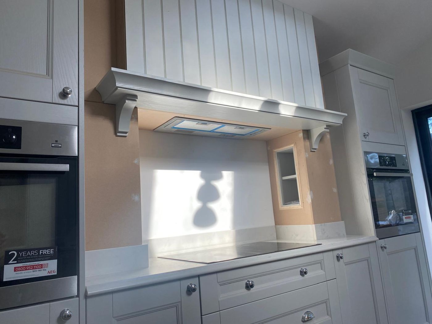 Light grey shaker kitchen with a tongue and groove canopy hood on corbels above the hob, ovens either side
