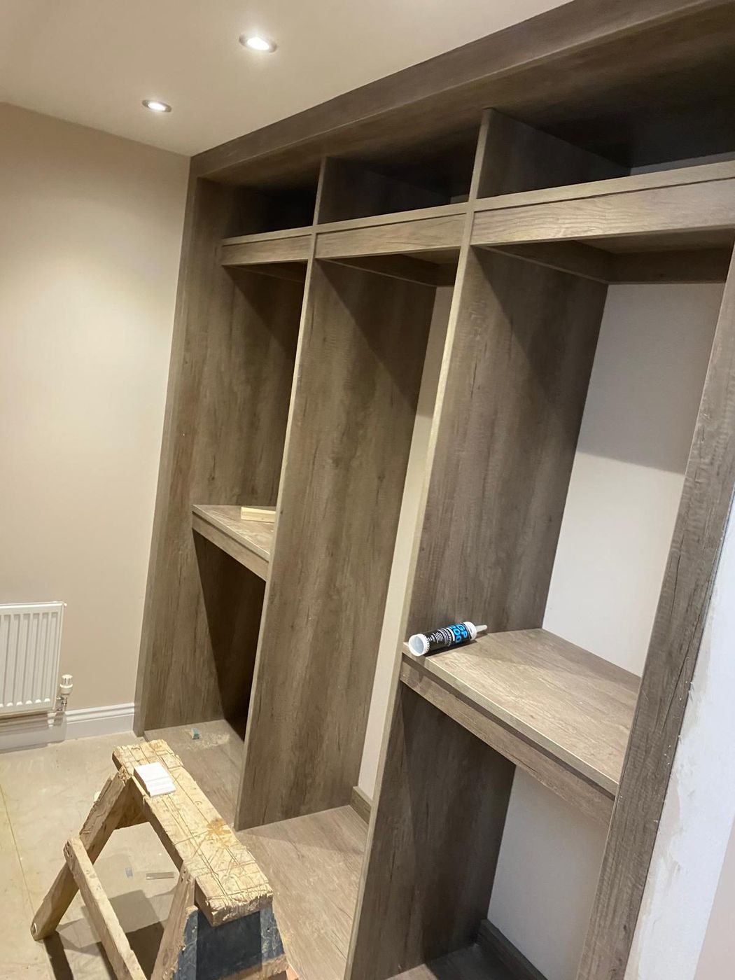 Built-in walk-in wardrobe frame in an oak-effect finish with open hanging sections, shelves and a top shelf run, before rails are fitted